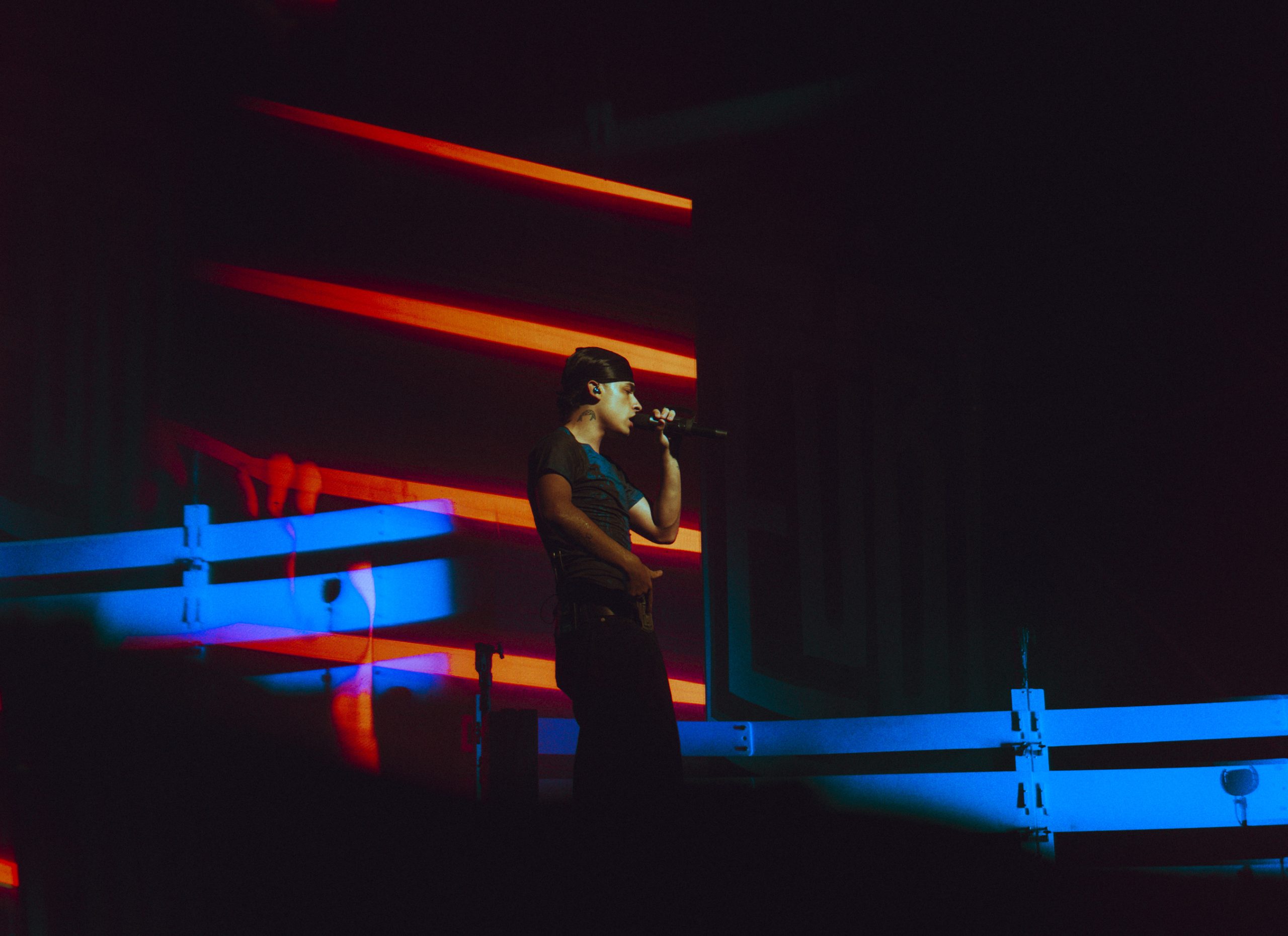 Trueno canta con un micrófono durante una actuación, iluminado por luces rojas y azules